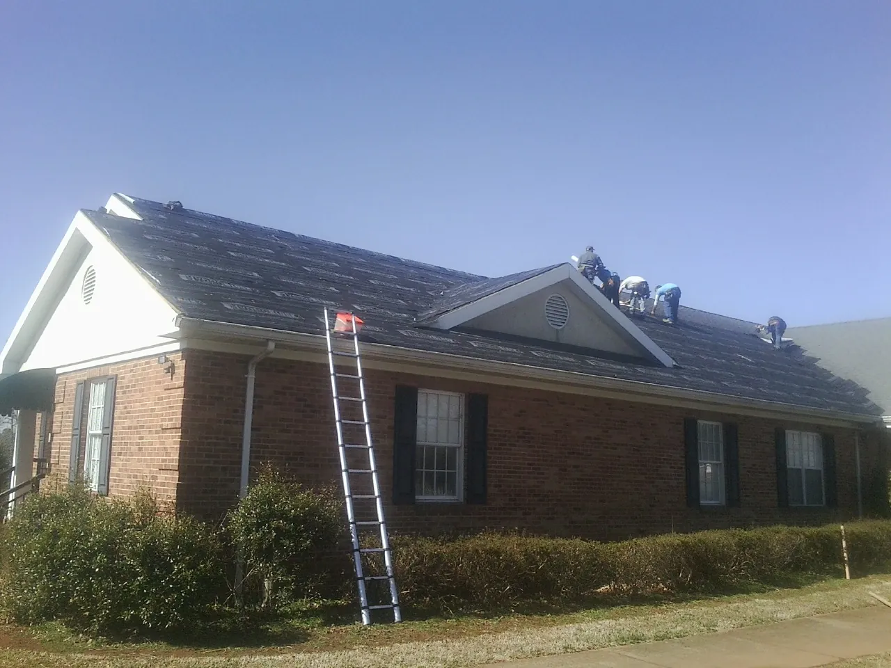 Crew tearing shingles off a brick ranch roof with a ladder set — Metal Roof Repair work by our crew in La Honda
