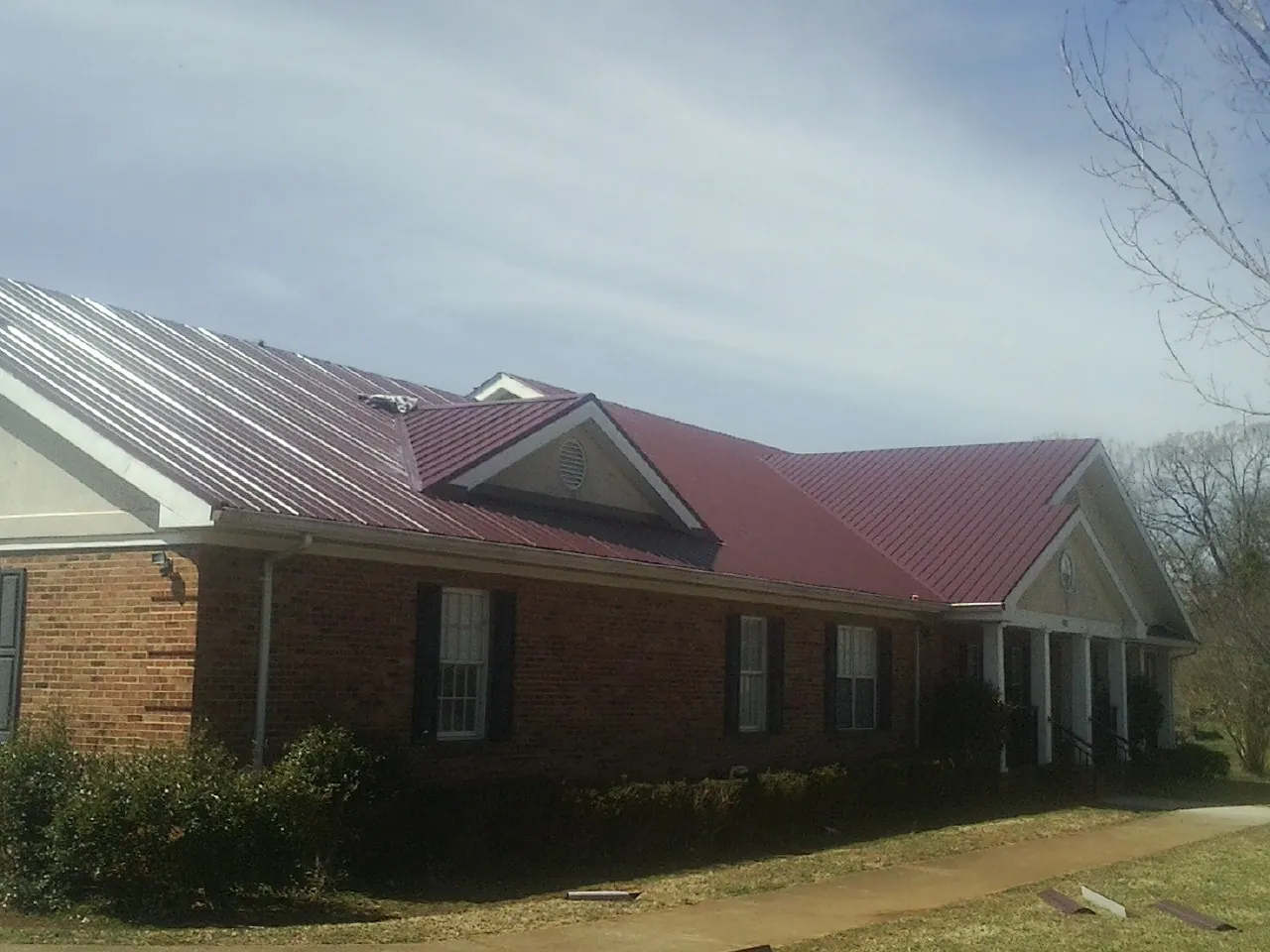 Red metal roof with gabled entries on a long brick building, from a Hail Damage Roof Repair job in La Honda