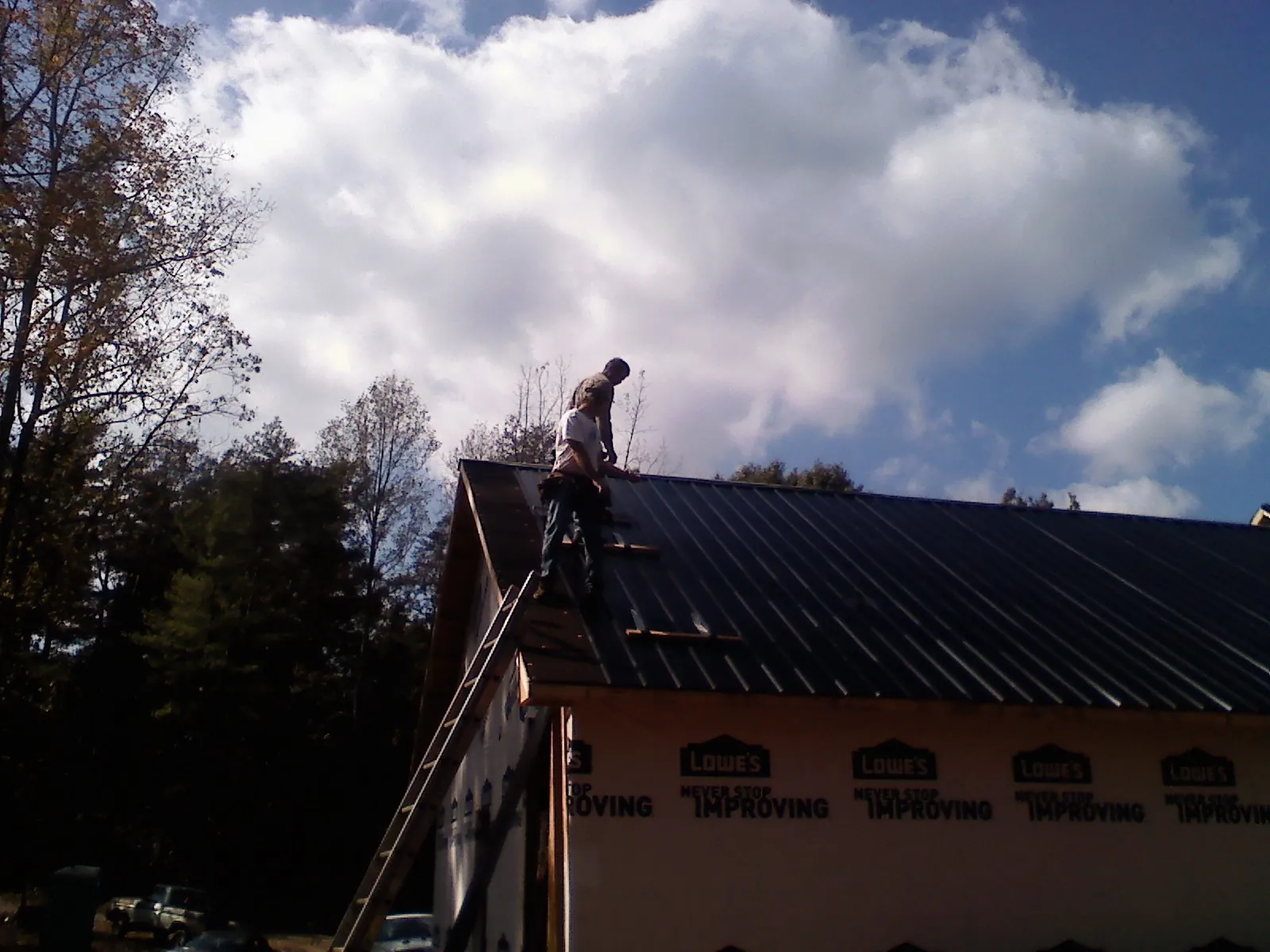 Roofer fastening dark metal panels high against a cloudy sky, from a Roof Inspection job in La Honda