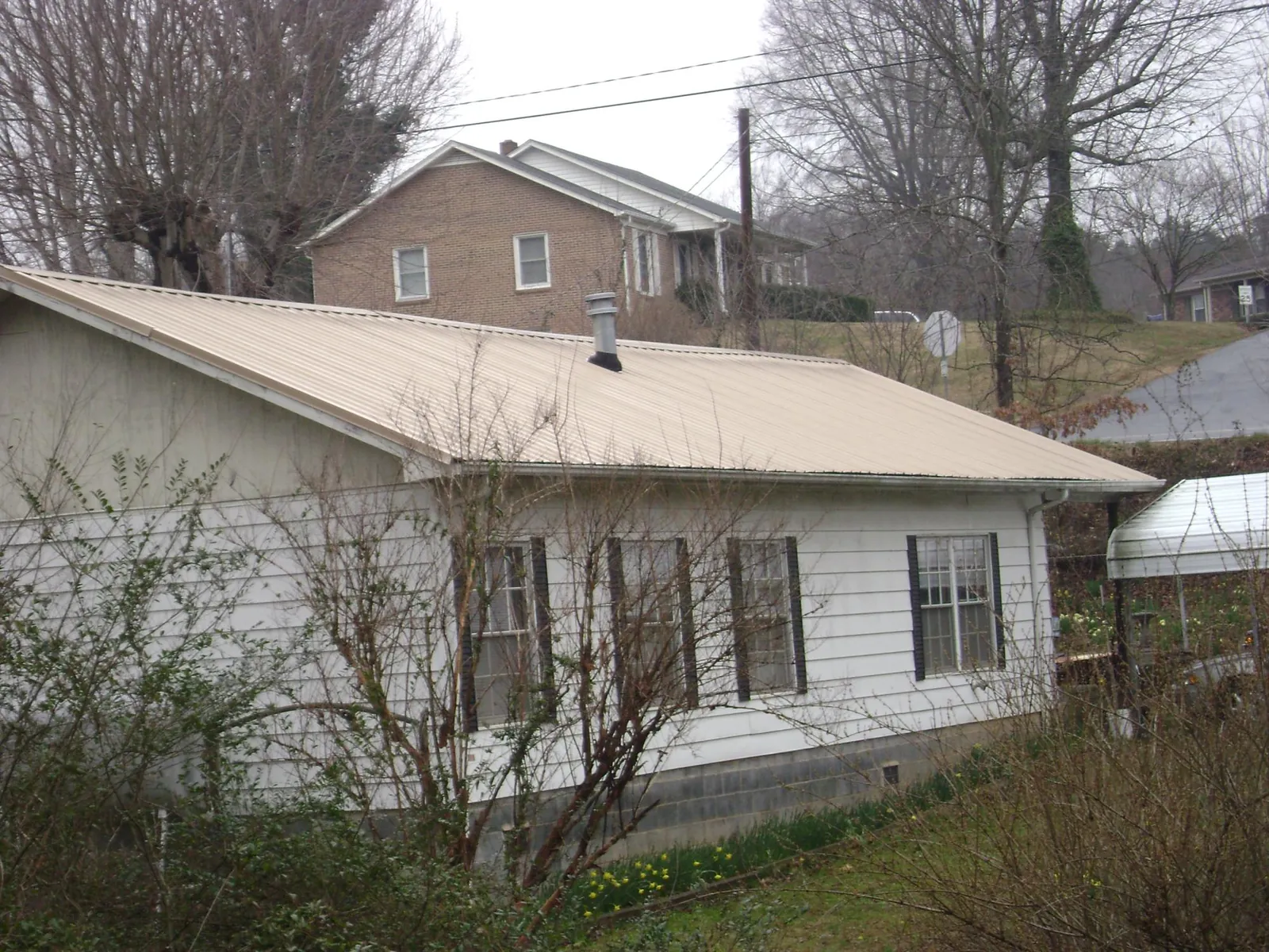 Tan metal roof on a white sided house set into a hillside — Commercial Roofing by Roofing Brothers in La Honda